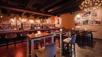 Elegant restaurantinterieur met donkerhouten elementen, bargedeelte en comfortabele stoelen in een gezellige sfeer.