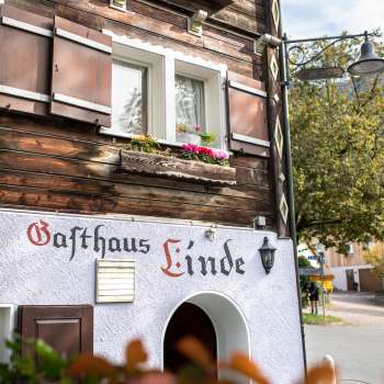 Gevel van Gasthaus Linde met rustieke houten constructie en luiken, versierd met bloemen.