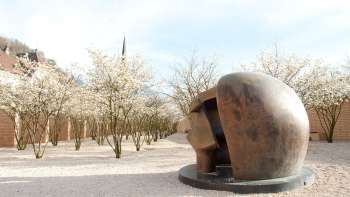 Bronzen sculptuur "Figure in a Shelter" van Henry Moore in het beeldenpark van Vaduz - omringd door bloeiende bomen in de lente.