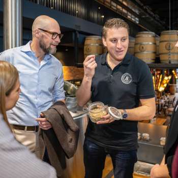 Een medewerker legt brouwingrediënten uit aan een groep geïnteresseerde gasten tijdens een rondleiding door de brouwerij.