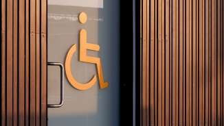 Oranje rolstoelsymbool op een glazen deur, wat wijst op een toegankelijk toilet, met houten lambrisering op de achtergrond.