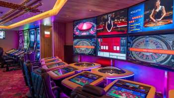 Moderne speeltafels met digitale schermen en verschillende roulette- en kaartspelopties in het sfeervol verlichte Casino Schaanwald.