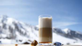 Glas latte macchiato op een houten schotel tegen de achtergrond van besneeuwde bergen