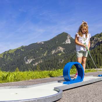 Meisje concentreert zich op een blauwe loopingbaan in een alpine omgeving tijdens het minigolfen