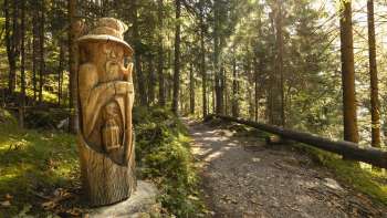 Houten figuur met lantaarn op "pad van de Walser legendes" in het mystieke boslicht