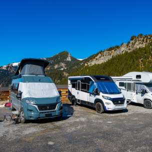 Meerdere campers en campers op een kampeerplaats in de bergen van Liechtenstein onder een strakblauwe hemel