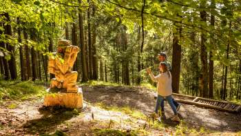 Twee wandelaars lopen langs een houten figuur op het "pad van de Walser legendes" .
