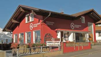 Rood gebouw van Restaurant Kainer met houten balkon en uitnodigende buitenruimte