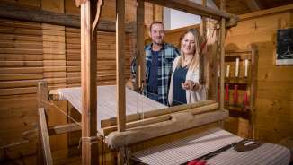 Een stel bekijkt een werkend historisch weefgetouw in het Walser Museum Triesenberg in Liechtenstein, omringd door houten lambrisering