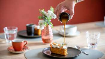 Dessert overgoten met karamelsaus, koffiekopjes en stijlvolle tafeldecoraties op de achtergrond