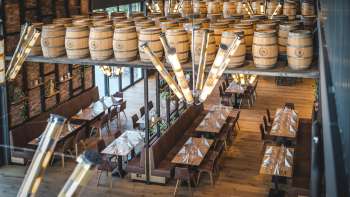 Uitnodigende brouwerijzaal met lange houten tafels, fustdecoraties en stijlvolle verlichting