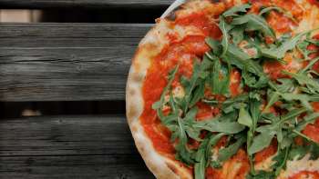 Verse pizza met tomatensaus en rucola, geserveerd op een rustieke houten tafel