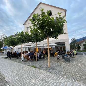 Levendig terras van St. Martins Pub am Platz met schaduwrijke bomen en gasten aan tafels.