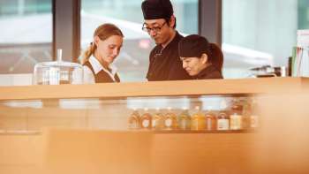 Drie medewerkers van het café in het Kunstmuseum werken samen aan de toonbank en wisselen ideeën uit.