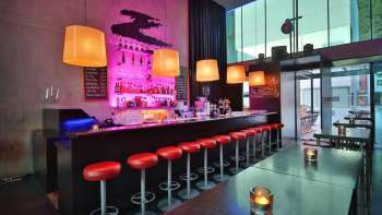 Moderne bar met lange toonbanken, rode barkrukken en stijlvolle verlichting in roze en oranje