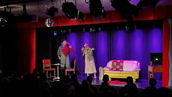 Cabaretscène bij K-BUM in Liechtenstein - kleurrijk podium met bank, acteursduo en publiek in de zaal.