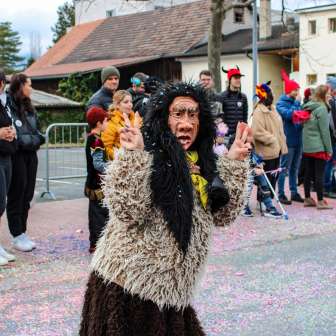 Vermomde Schaanse heks tijdens de carnavalsoptocht in Schaan, Liechtenstein, voor publiek en kleurrijke confetti op straat