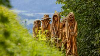 Houten figuren op het Walser sagenpad in Triesenberg Detailopname van gebeeldhouwde houten figuren in mystieke uitbeelding op het Walser Legendepad in Triesenberg, omgeven door groene natuur