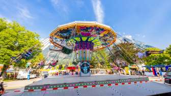 Grote kleurrijke kettingcarrousel op de kermis in Balzers, vol gelukkige bezoekers voor een bergdecor onder een blauwe hemel.