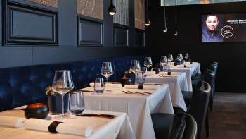 Elegant interieur van de Esquire Bar & Bistro in Vaduz met stijlvol gedekte tafels, donkerblauw gestoffeerde bank en sfeervolle verlichting.