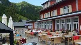 Zonnig terras van het restaurant met overdekte tafels, parasols en uitzicht op de Alpen.