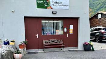 Ingang van de boerderijwinkel Aeulehof met rood hek, bankje en bloemdecoraties in Triesen, Liechtenstein.