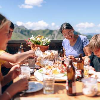 Gezin luncht samen op een zonnig terras in Sarreis, omringd door bergen en regionale specialiteiten