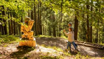 Twee wandelaars lopen langs een houten figuur op het "pad van de Walser legendes" .