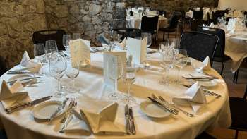 Elegant gedekte ronde tafel met witte tafelkleden, servetten en menu's voor een stenen muur.