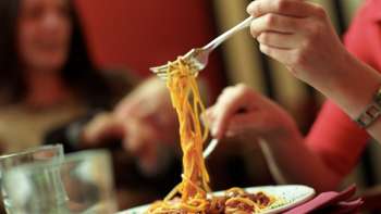 Een persoon tilt spaghetti van een bord met een vork in de Brasserie Burg - Italiaans genieten in een gezellige sfeer.