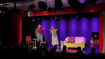 Cabaretscène bij K-BUM in Liechtenstein - kleurrijk podium met bank, acteursduo en publiek in de zaal.