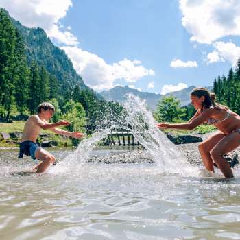 Kinderen spetteren in het Gänglemeer bij Steg, omgeven door bossen en bergen - ervaar de natuur en zoek verkoeling in Liechtenstein