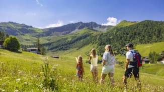 Een gezin wandelt door een bloeiende zomerweide in Malbun, Liechtenstein, en geniet van het uitzicht op de omringende Alpen.