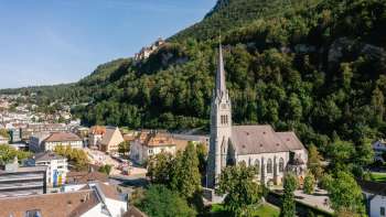 Luchtfoto van de Sint-Florinakathedraal in Vaduz met het kasteel van Vaduz op de achtergrond op een zonnige dag.