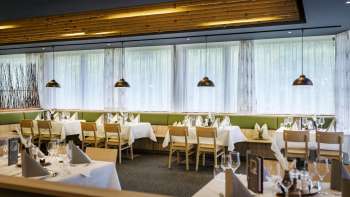 Een uitnodigende eethoek met ronde tafels en zachte groene stoelen, ingericht in een moderne, natuurlijke stijl.