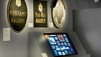 Museumzaal met oude postborden en een digitale display over de geschiedenis van het postkantoor in Liechtenstein.