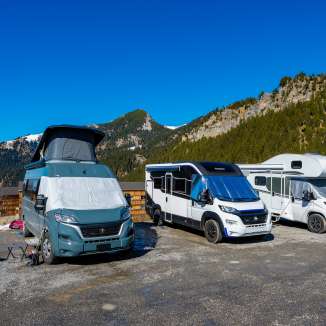 Meerdere campers en campers op een kampeerplaats in de bergen van Liechtenstein onder een strakblauwe hemel