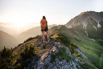 Vrouw met rugzak geniet van de zonsopgang tijdens een wandeling in Malbun met uitzicht op het berglandschap