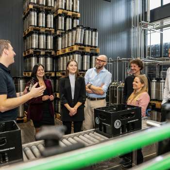Groep bezoekers tijdens een rondleiding door het vatenmagazijn van de brouwerij met uitleg van een brouwerijmedewerker.