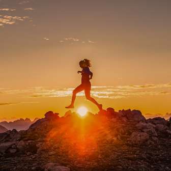 Twee trailrunners steken een rotsachtige bergrug over bij zonsopgang in Liechtenstein, in het gouden licht van de dageraad