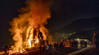 Groot vreugdevuur in Liechtenstein bij nacht, mensen kijken naar het laaiende vuur op een heuvel met uitzicht op de verlichte stad en de bergen.