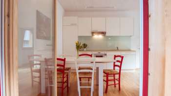 Lichte woon- en eetruimte met moderne kitchenette en rode en witte stoelen in het gastenverblijf op Camping Mittagsspitze.