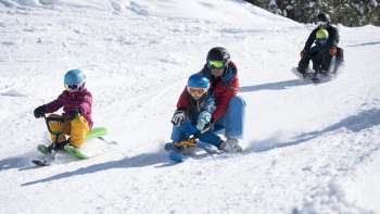 Gezinsvriendelijk rodelplezier op de besneeuwde rodelbaan in Malbun - kinderen en volwassenen genieten van de afdaling in het Liechtensteinse winterparadijs.