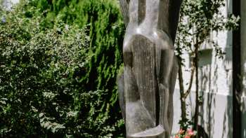 Modern bronzen beeld, staand tussen bloemen en struiken in Vaduz - werk van Herbert Albrecht.