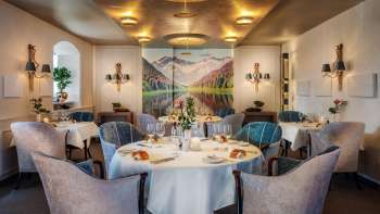 Een elegante eetzaal met stijlvol gedekte tafels, een chique sfeer en een groot landschapsschilderij