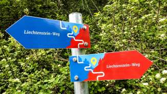 Kleurrijke wegwijzer van het "Liechtenstein-Weg" met rode en blauwe pijlen tegen een groene bosachtergrond
