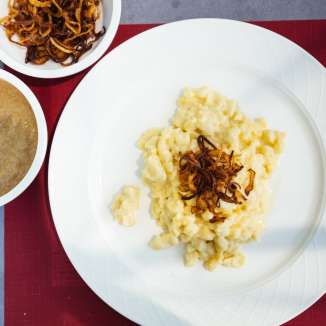 Traditionele Käsknöpfle met gebakken uien en appelmoes uit Liechtenstein op een wit bord