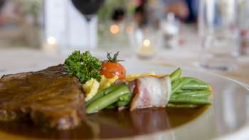 Close-up van een hoofdgerecht met groene groenten, spek en romige saus op het bord