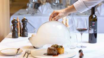 Gourmetschotel geserveerd met vlees en bijgerecht, decoratief opgesteld onder een witte cloche in het elegante Alpspitz restaurant.