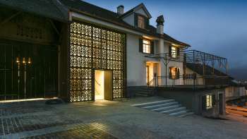Modern verlicht Kulturhaus Rössle in Mauren bij schemering, met glazen gevel, historische gebouwuitbreiding en geplaveid voorplein.